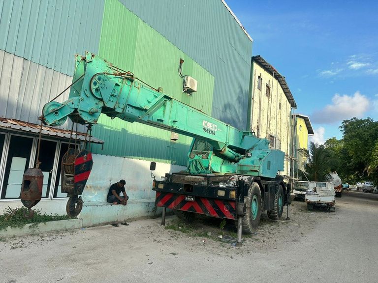Rough-terrain crane parked beside a warehouse